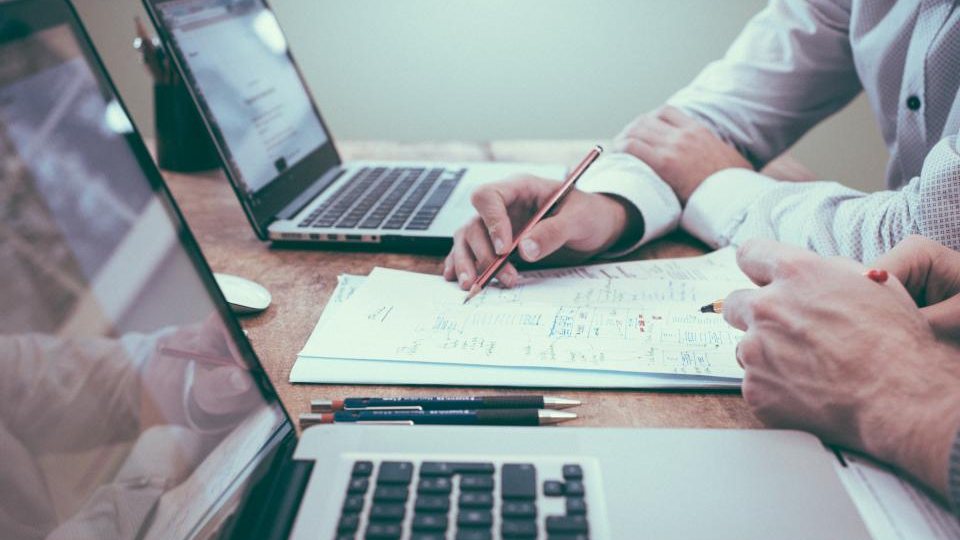 Hai người trao đổi bên bản vẽ quy trình và máy tính xách tay