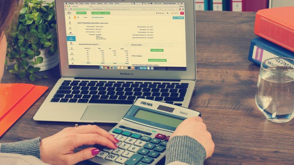 Bàn tay bấm máy tính cầm tay bên cạnh máy tính xách tay hiển thị bảng tính